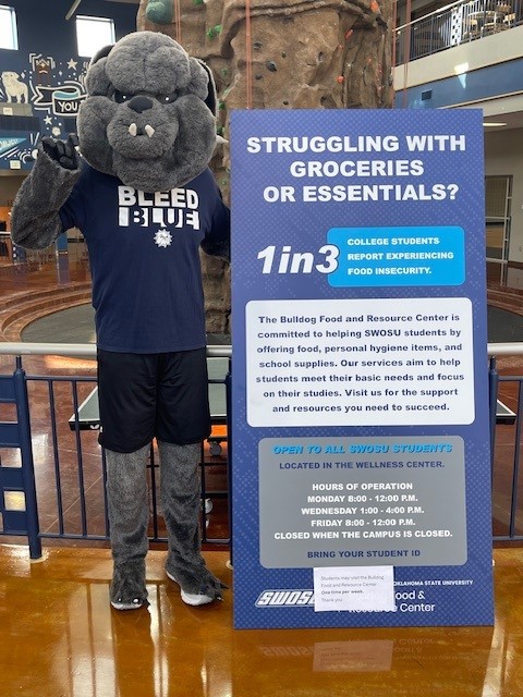 Bulldog standing by sign in wellness center that says: STRUGGLING WITH GROCERIES OR ESSENTIALS? 1in3 COLLEGE STUDENTS REPORT EXPERIENCING FOOD INSECURITY. The Bulldog Food and Resource Center is. committed to helping SWOSU students by offering food, personal hygiene items, and school supplies. Our services aim to help students meet their basic needs and focus on their studies. Visit us for the support and resources you need to succeed. OPEN TO ALL SWOSU STUDENTS LOCATED IN THE WELLNESS CENTER. HOURS OF OPERATION MONDAY 8:00 - 12:00 P.M. WEDNESDAY 1:00-4:00 PM. FRIDAY 8:00-12:00 P.M. CLOSED WHEN THE CAMPUS IS CLOSED. BRING YOUR STUDENT ID