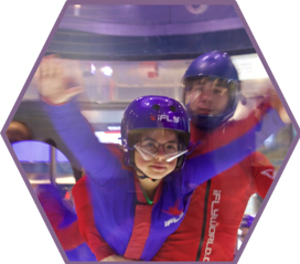 A camper flies in the wind tunnel at iFly indoor skydiving experience.  She is assisted by an iFLY employeer.